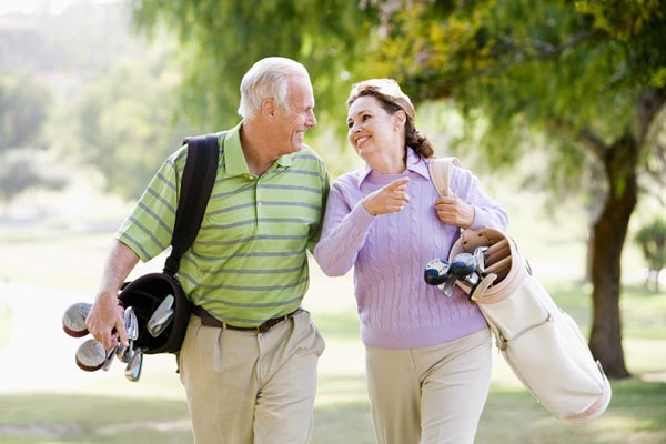 An older couple laughing as they to the next hole with their golf clubs.