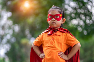 A girl in a red mask and cape, pretending to be a superhero.