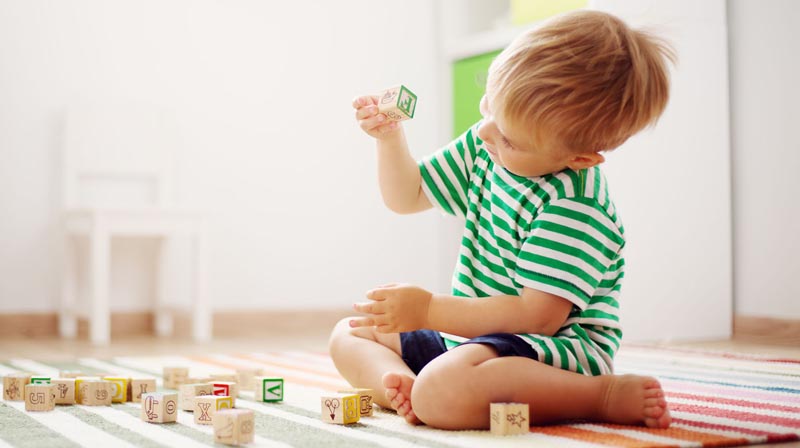 A toddler surrounded by alphabet blocks, examining one closely.