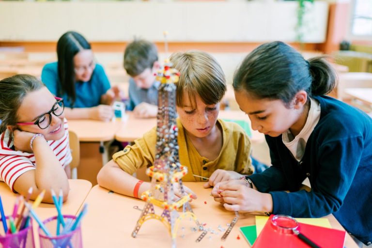 Three schoolchildren working together to build a model of the Eiffel Tower using a metal construction kit.