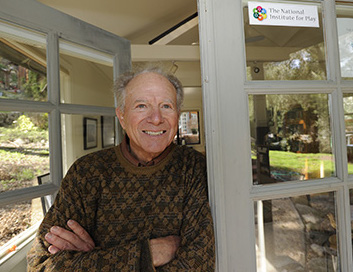 A man with graying hair and a bright smile leans casually against an open French door.