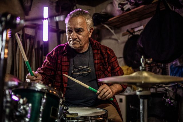 An older man deeply engaged in playing a drum set in his garage.