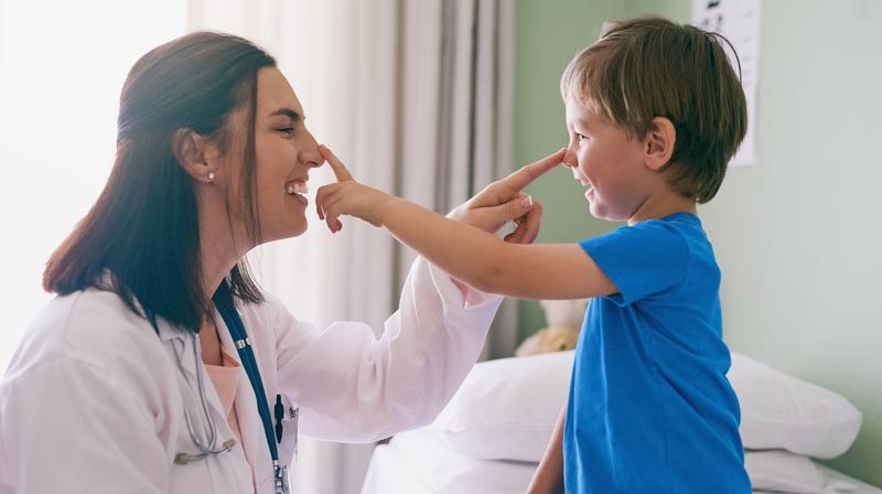 A doctor and her preschooler patient playfully touching each other's noses.